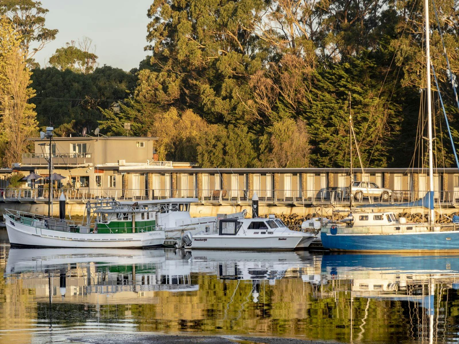 Boats moored on river in foreground with motel in background with large gum trees behind motel
