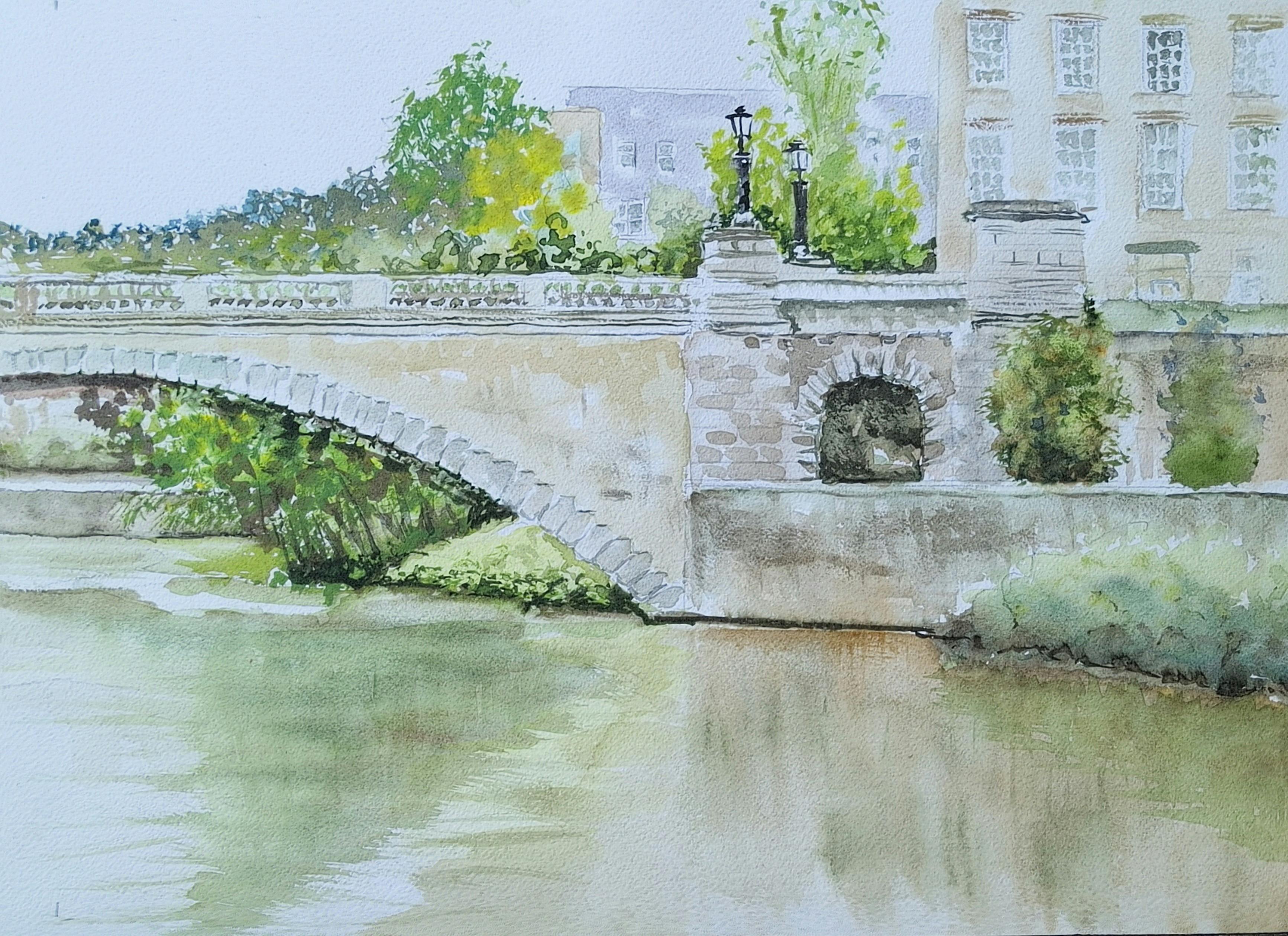 View across the water in Bath UK with a stone bridge and  trees and grass to the water's edge