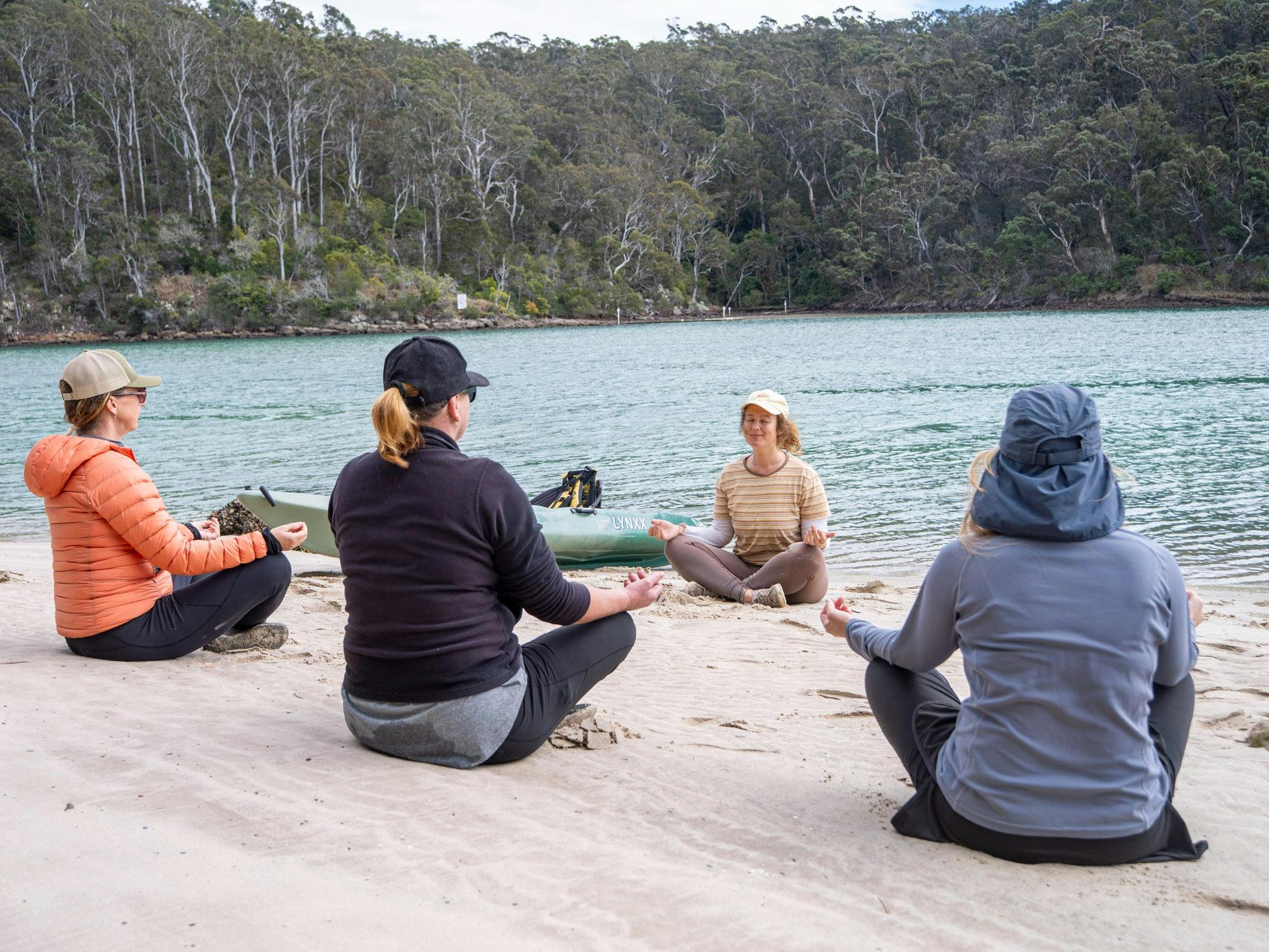 3 guests following guided breath techniques on the beach with the river in the background