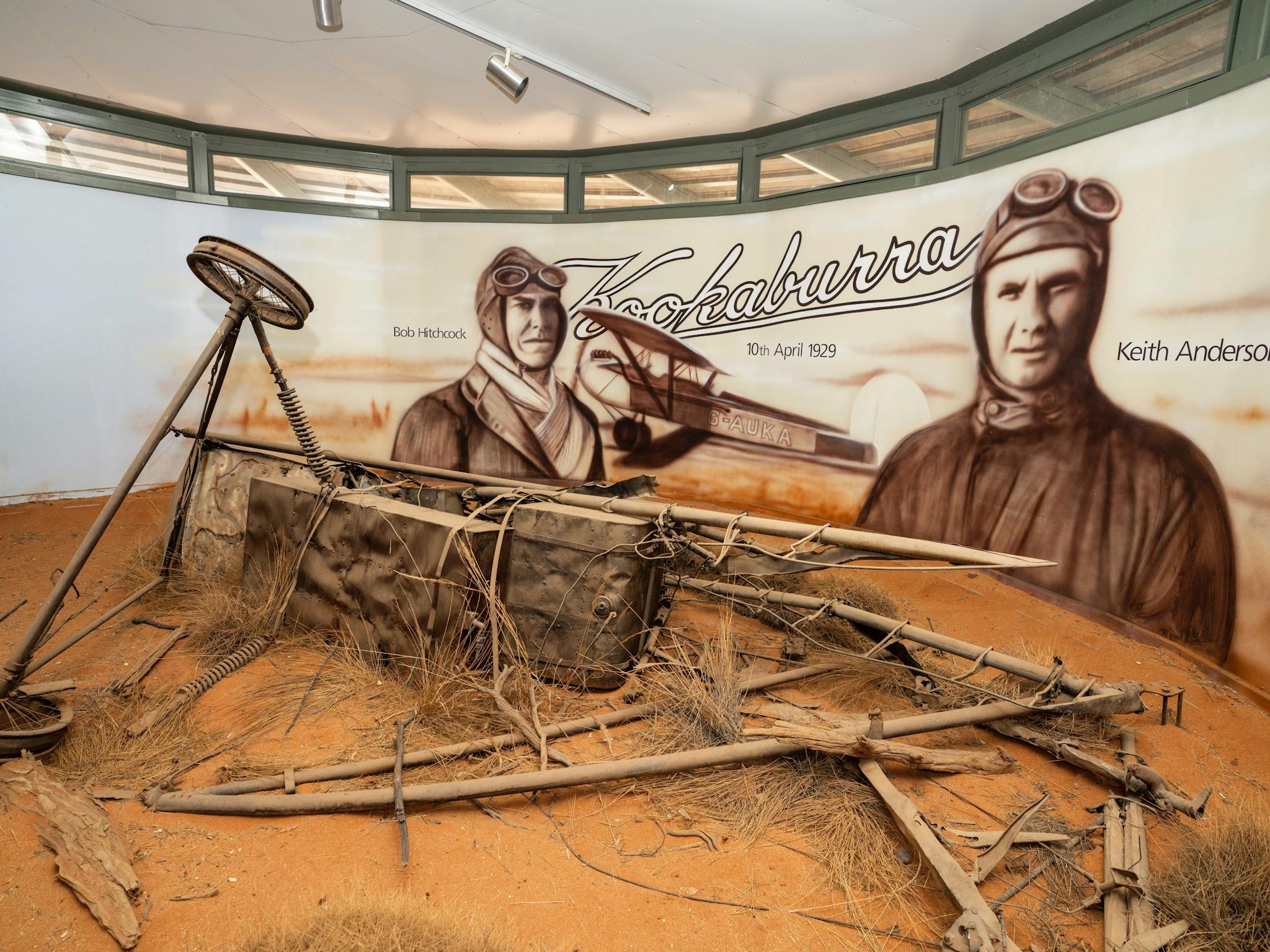 Portraits of Hitchcock and Anderson behind remains of their plane in diorama