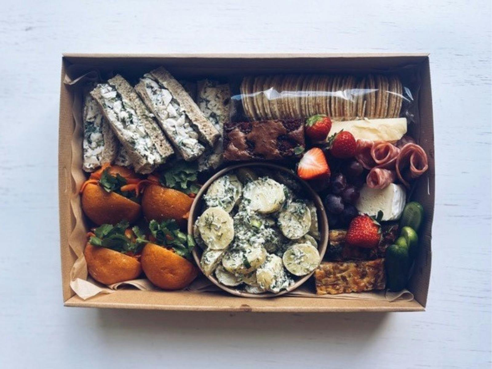 Cheese, antipasto and fruits placed in a brown cardboard box.
