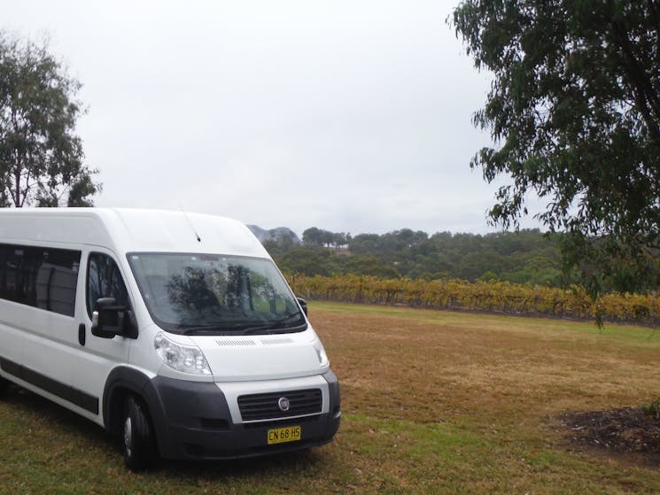 A Shepherd Small Bus is parked on the grass with a vineyard in the background
