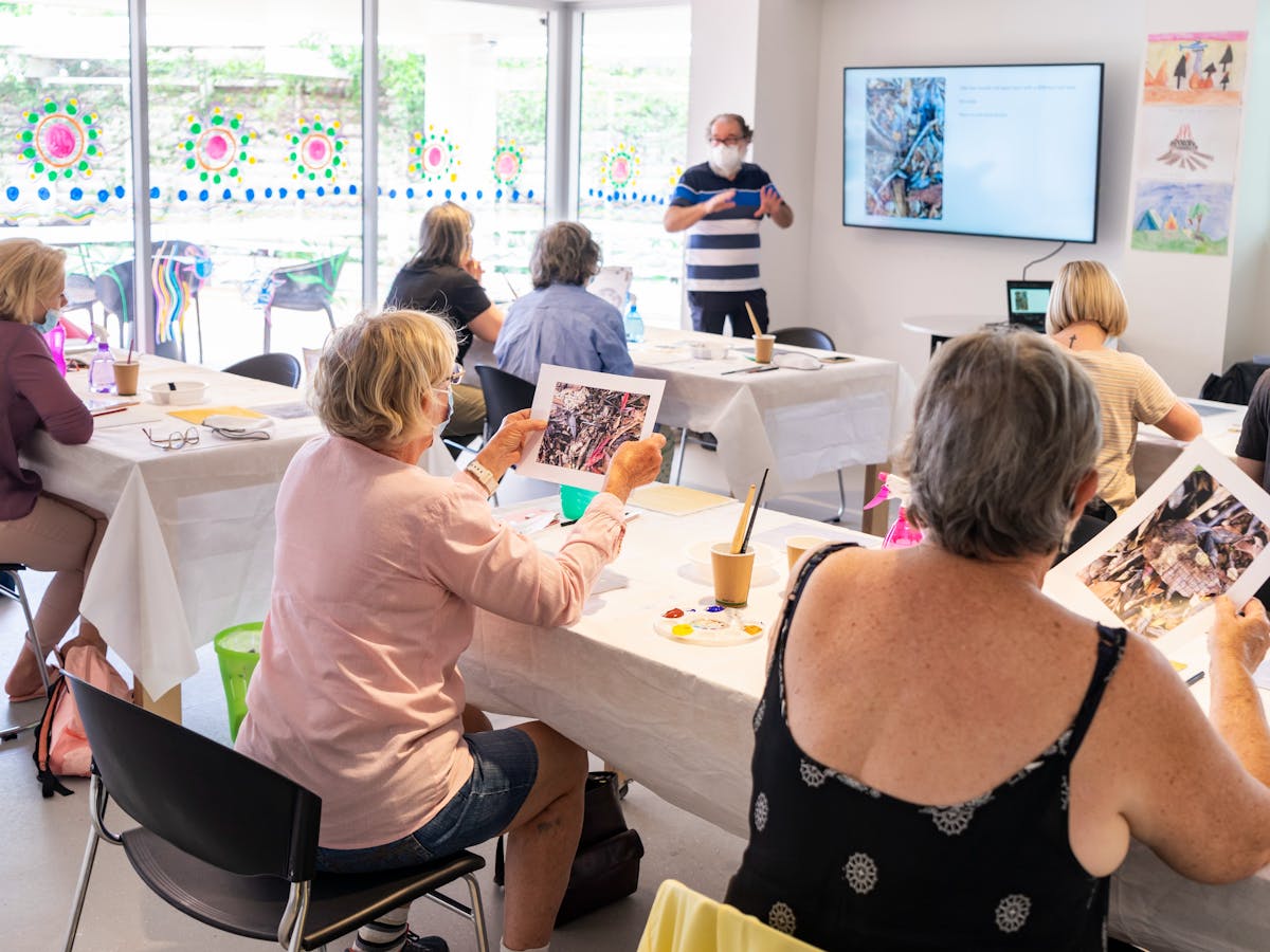 Large group of people sitting at table participating in 'John A. Robinson: Being' art workshop