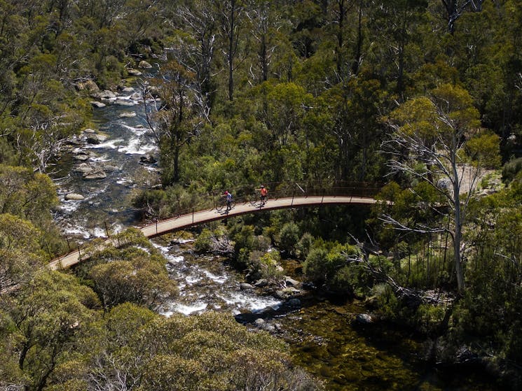 Aerial view of two bike riders crossing a bridge on Thredbo Valley track, Kosciuszko National Park