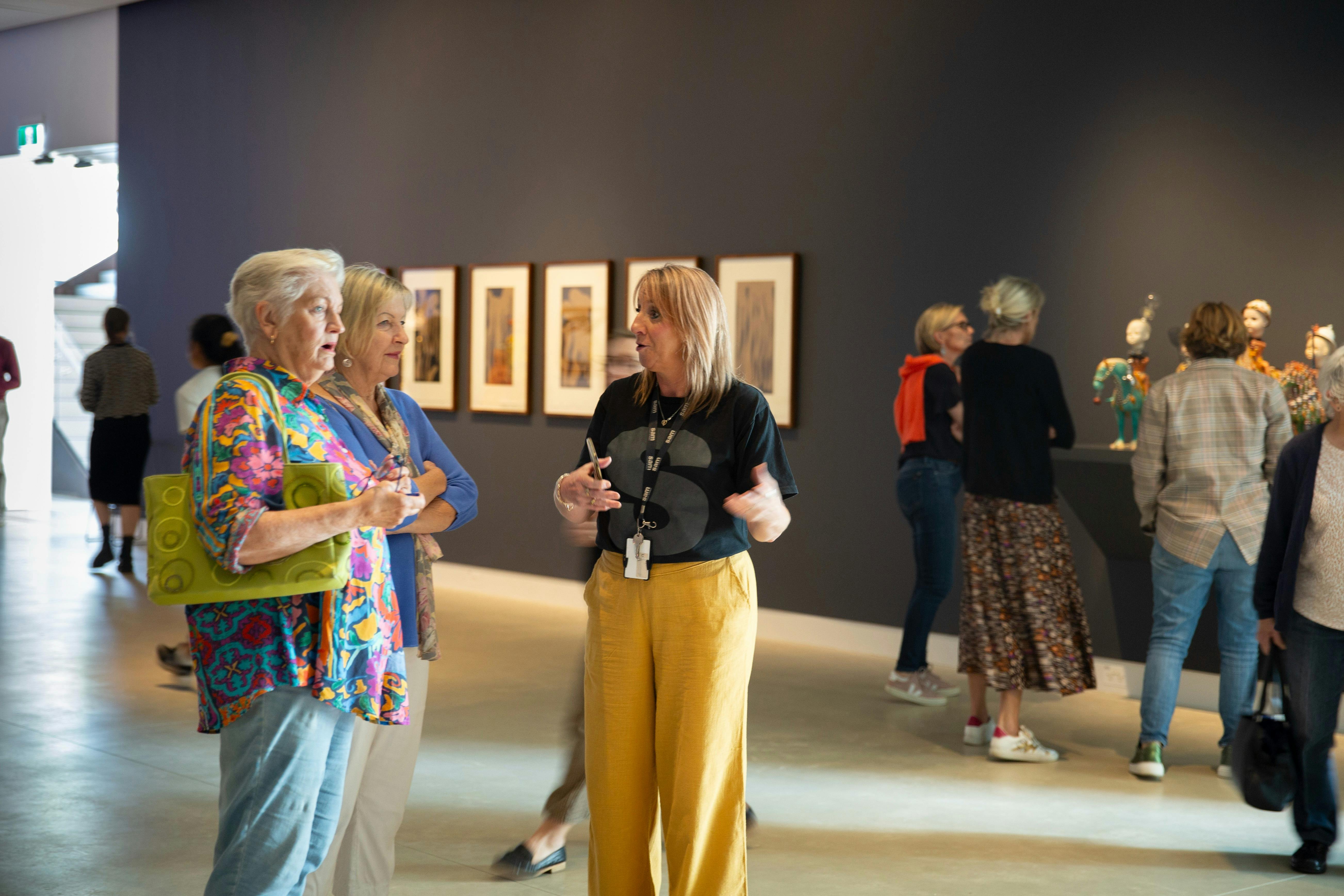 A staff member converses with two senior women in an art gallery