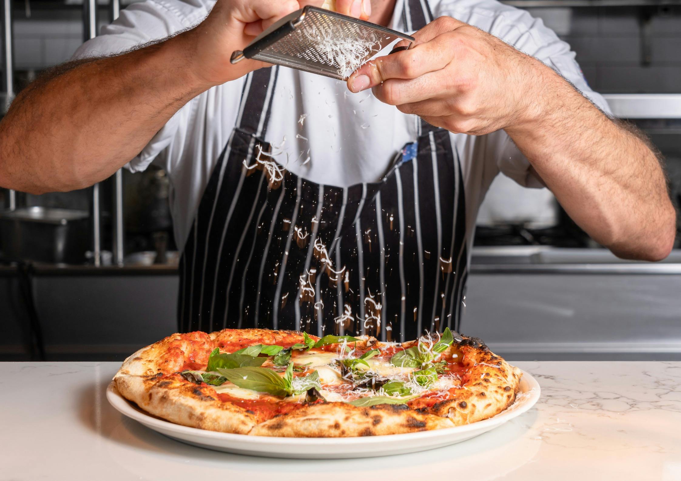 a chef grating cheese on top of a pizza