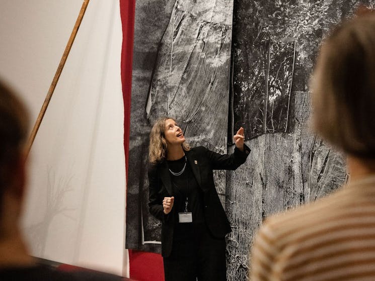 A tour guide standing in front of a large hanging artwork discussing the work with visitors