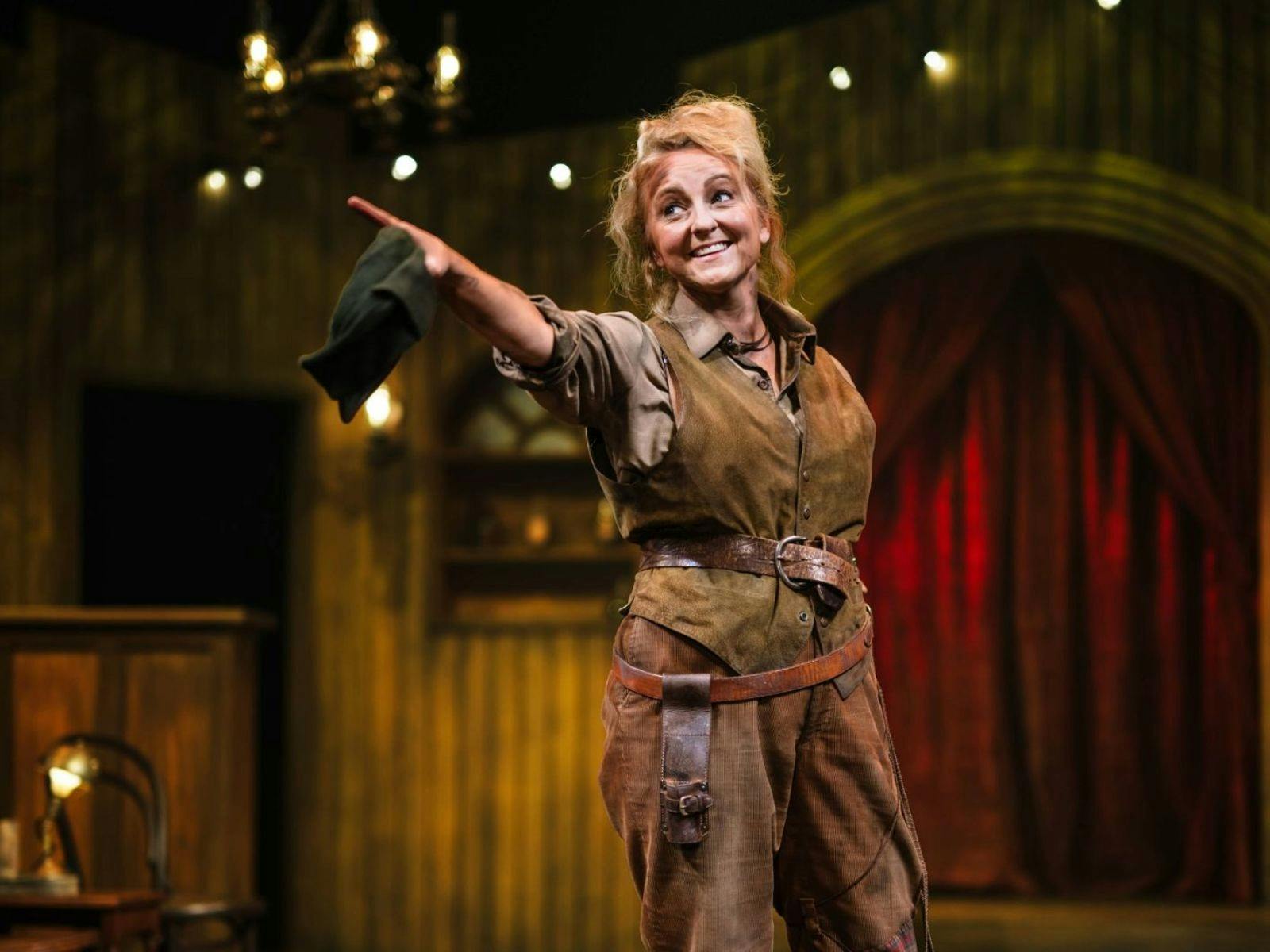 Women with blonde hair dressed in brown dirty pants with a knife belt and vest with a belt pointing Women with blonde hair dressed in brown dirty pants with a knife belt and vest with a belt pointing