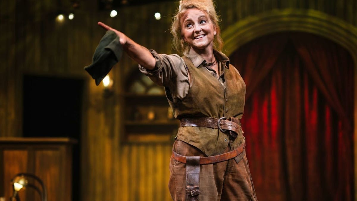 Women with blonde hair dressed in brown dirty pants with a knife belt and vest with a belt pointing