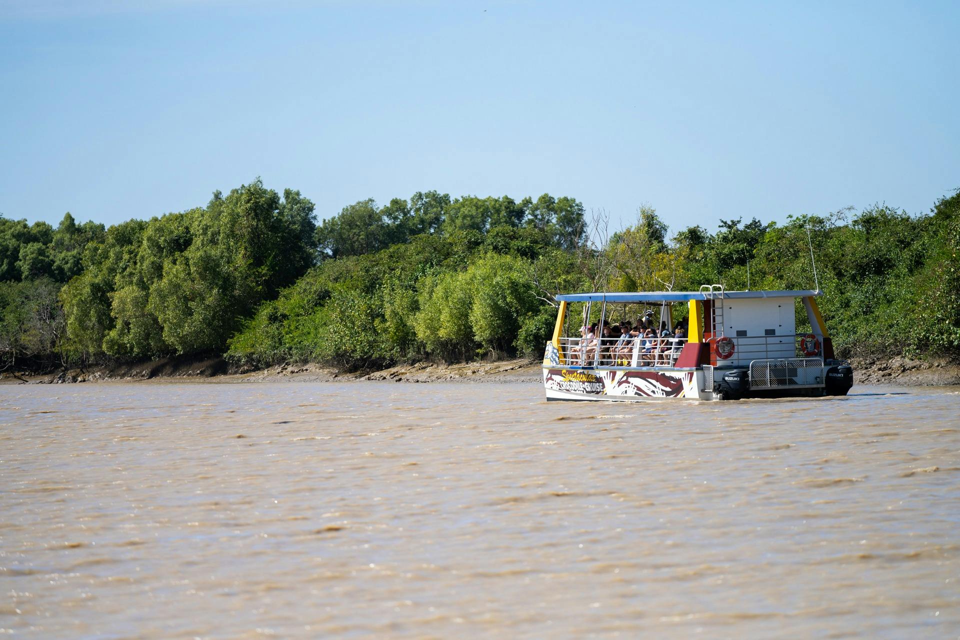 A large branded catamaran cruises down the Adelaide River at a distance