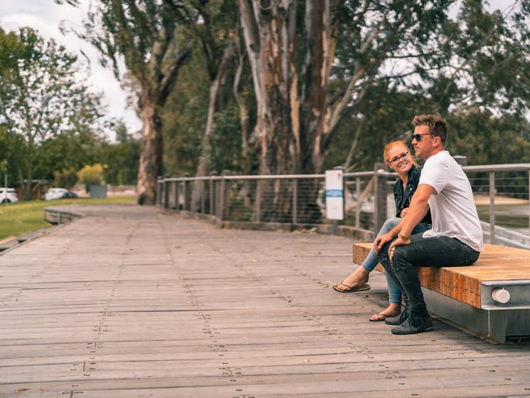 Couple sitting on a wooden boardwalk over looking the river