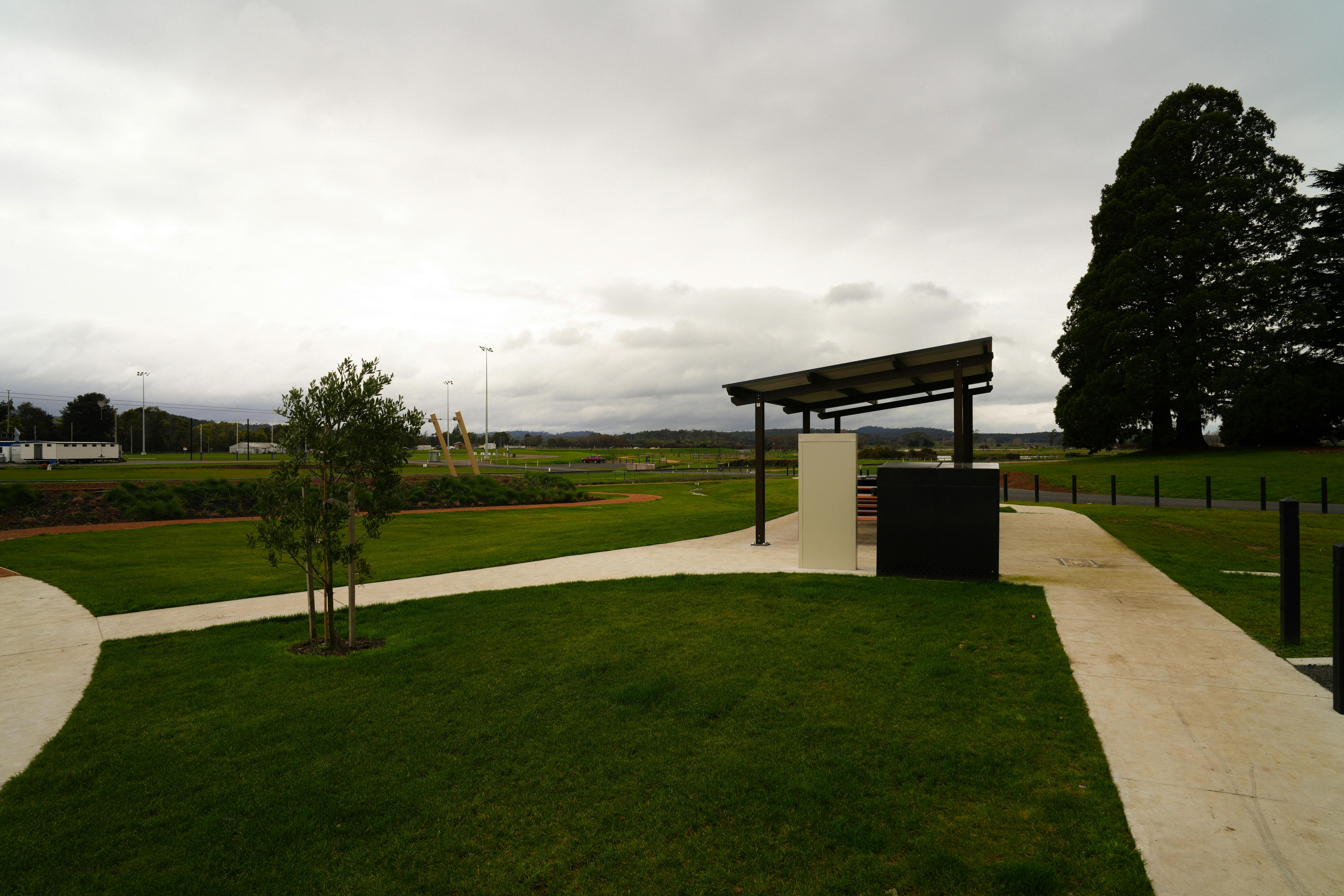 A shelter with a path leading around it. Inside is  BBQ and two tables