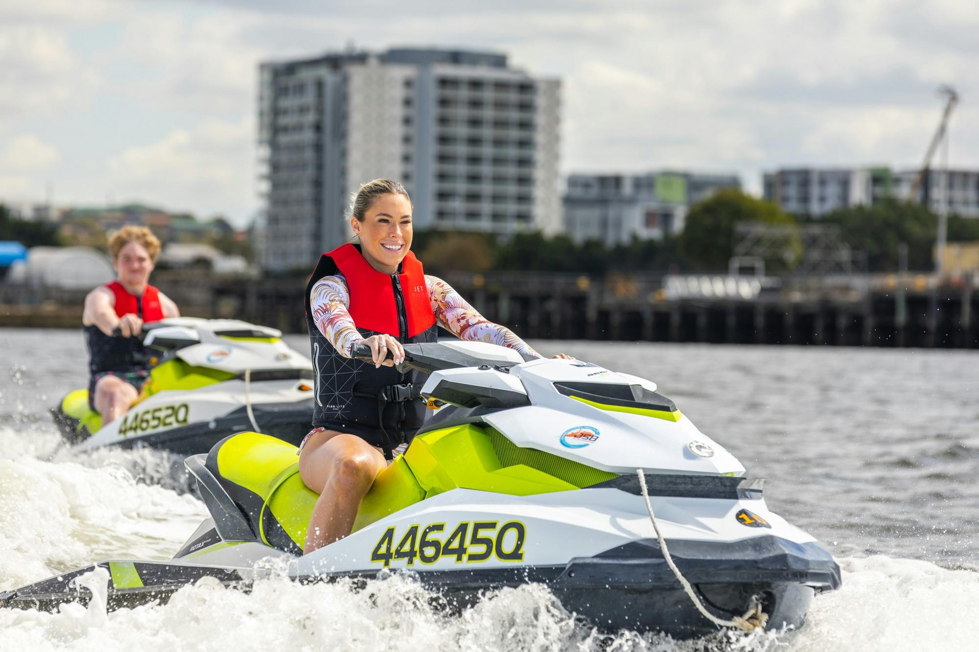 Female on a jet ski smiling with Brisbane City skyline in background.