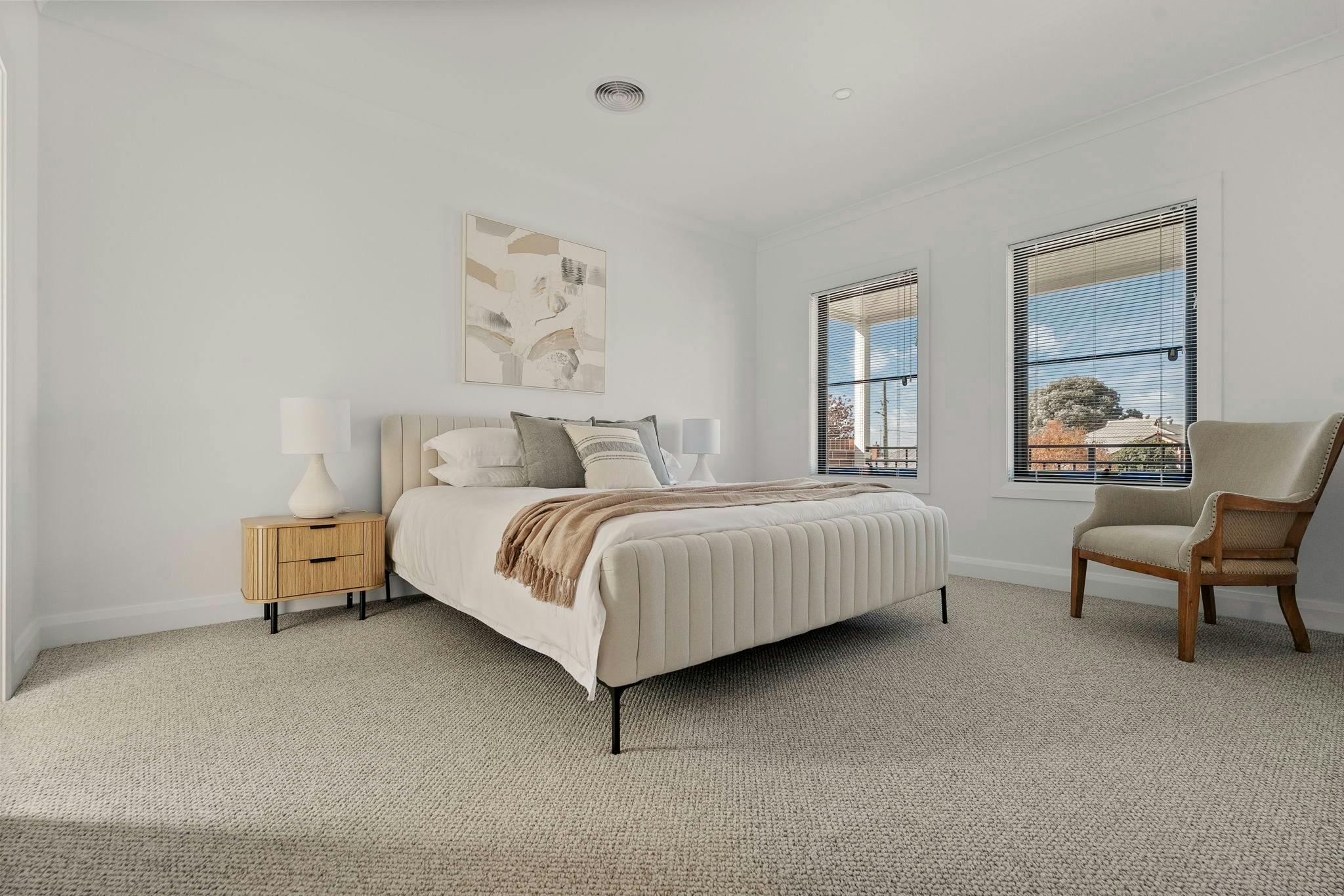 Main bedroom with king bed, carpet, side tables, 2 windows, armchair