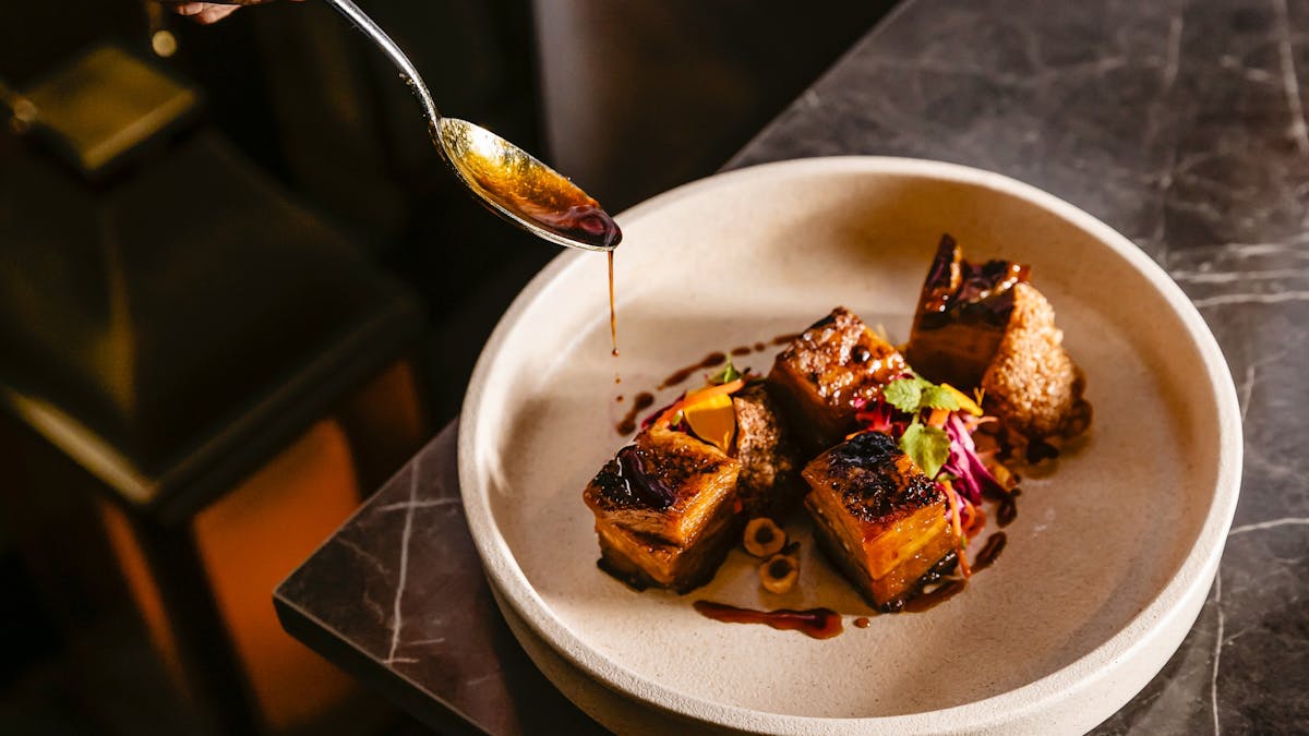 Twice Cooked Pork Belly on a white plate on the edge of a table