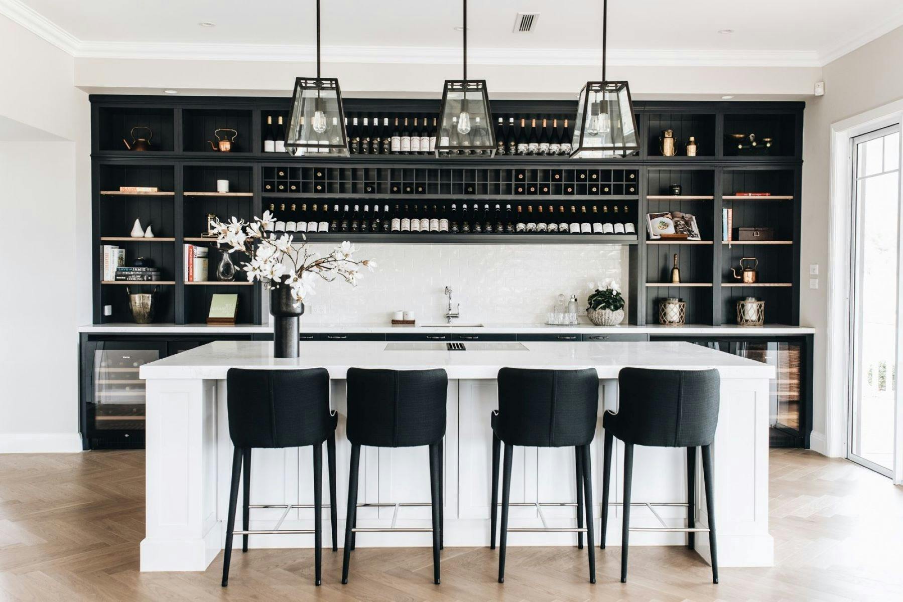 Image of the Saddle Ridge kitchen. Large stone benchtop is a feature. Wine wall in background.
