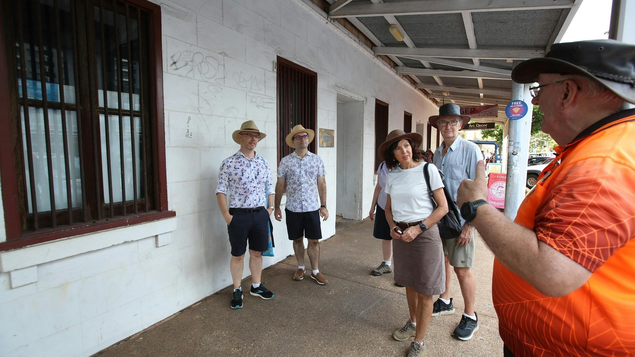 Walk Darwin tour group stands before an old building displaying white stucco and bars on windows