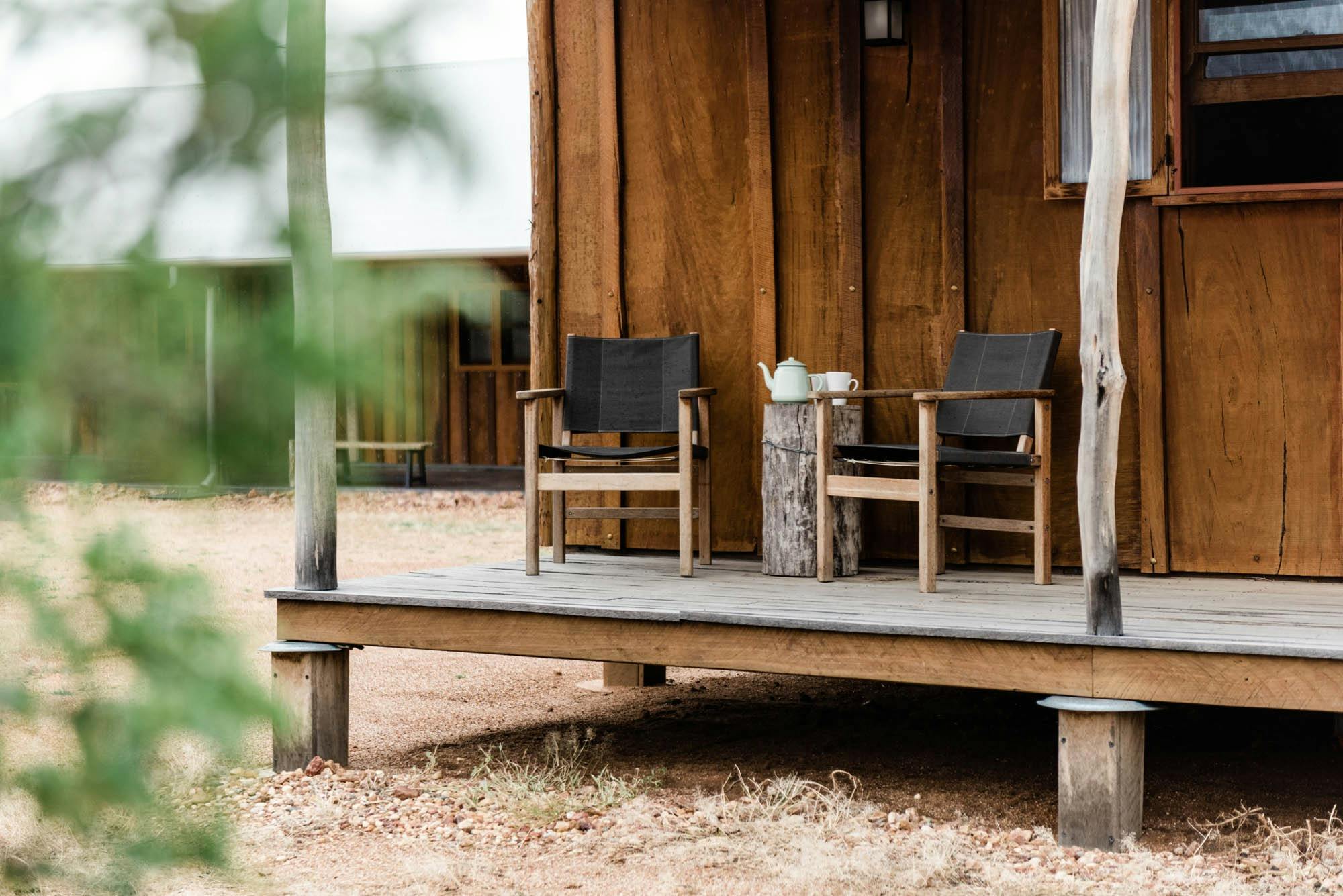 Canvas chairs on timber verandah with tea pot and cup on stump of wood used as table