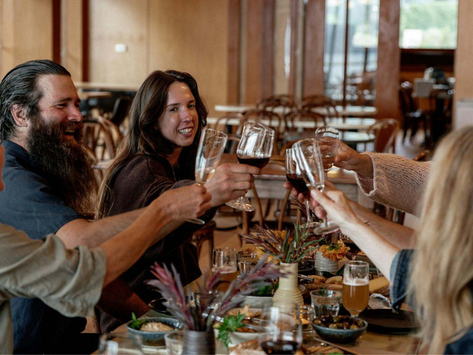 Group of friends toasting with wine at a long table laden with food.