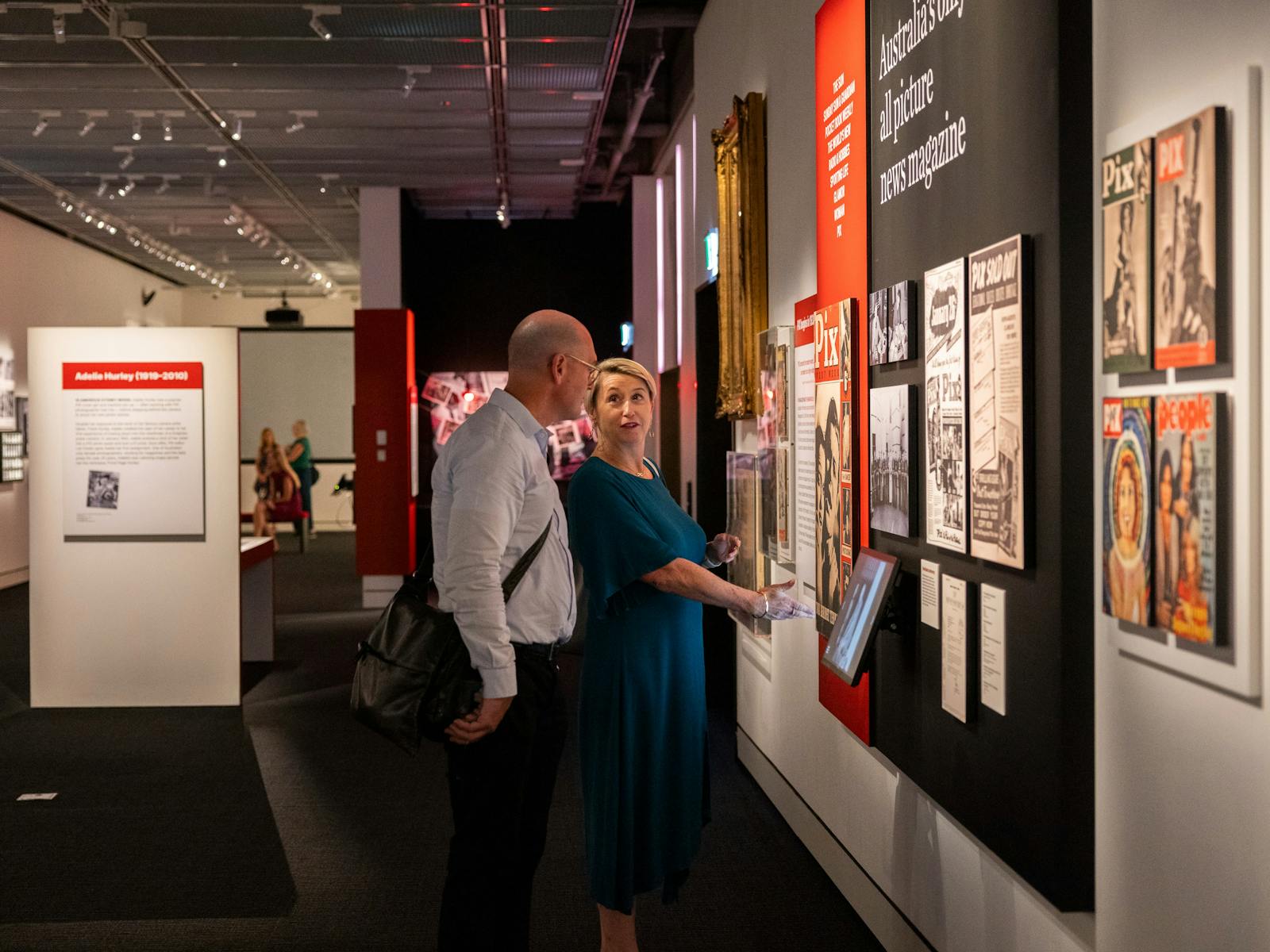 Two people in a exhibition with magazine covers and photography on display