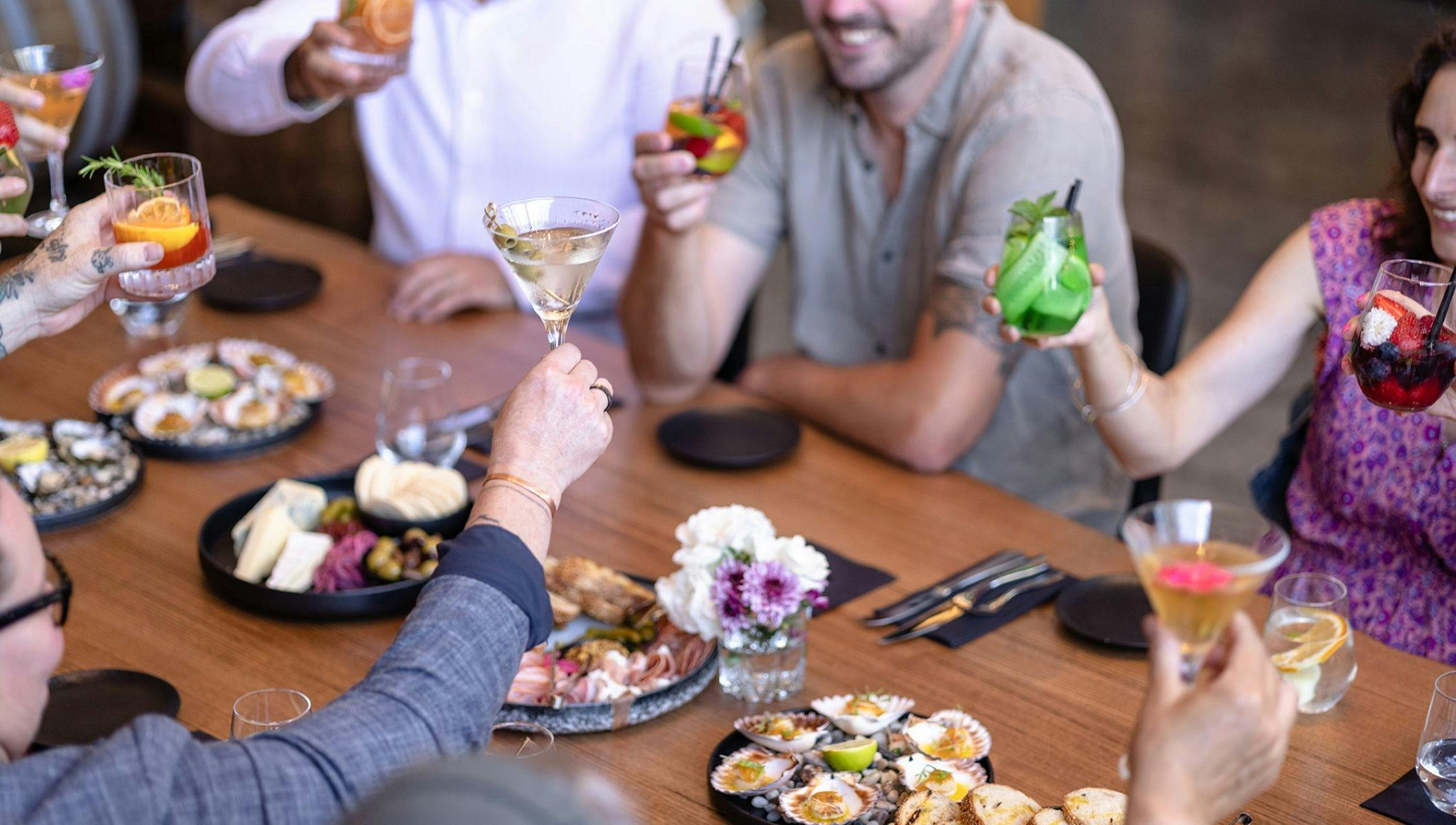 Four people sitting around a table with various meals, each holding a drink to cheers