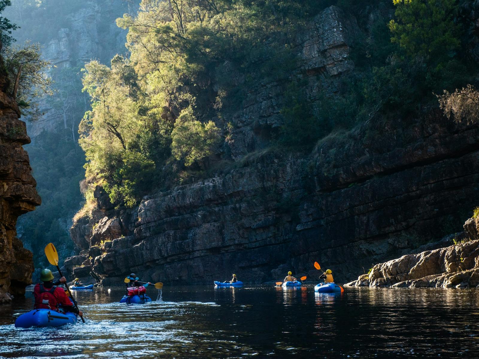 Packrafters paddle through a gorge with morning sun in the trees
