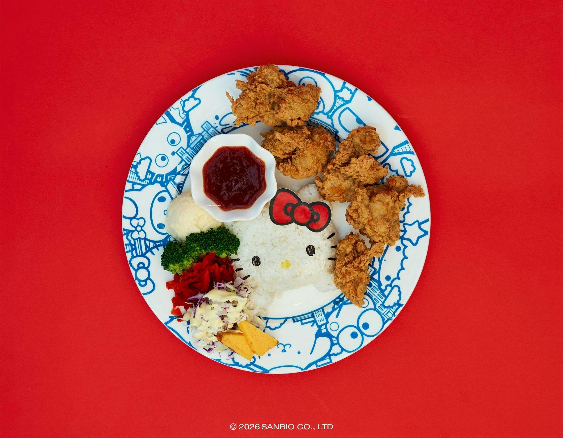 Plate of fried chicken, veggies, and Hello Kitty-shaped rice with a red bow on a red background.