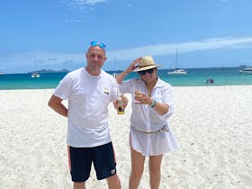 A couple holding drinks saying cheers on Whitehaven Beach