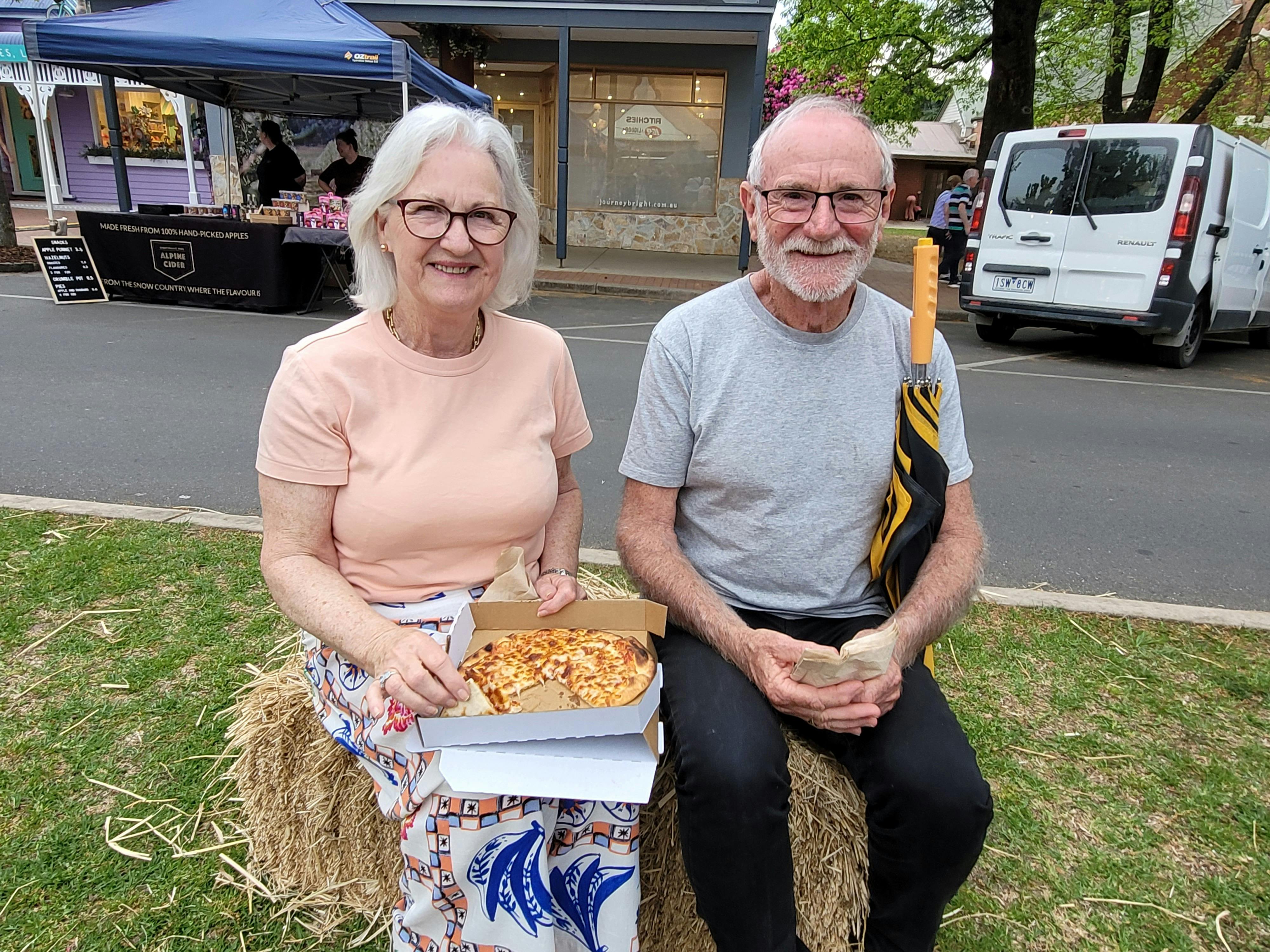 two people sitting on hay bales enjoying pizza