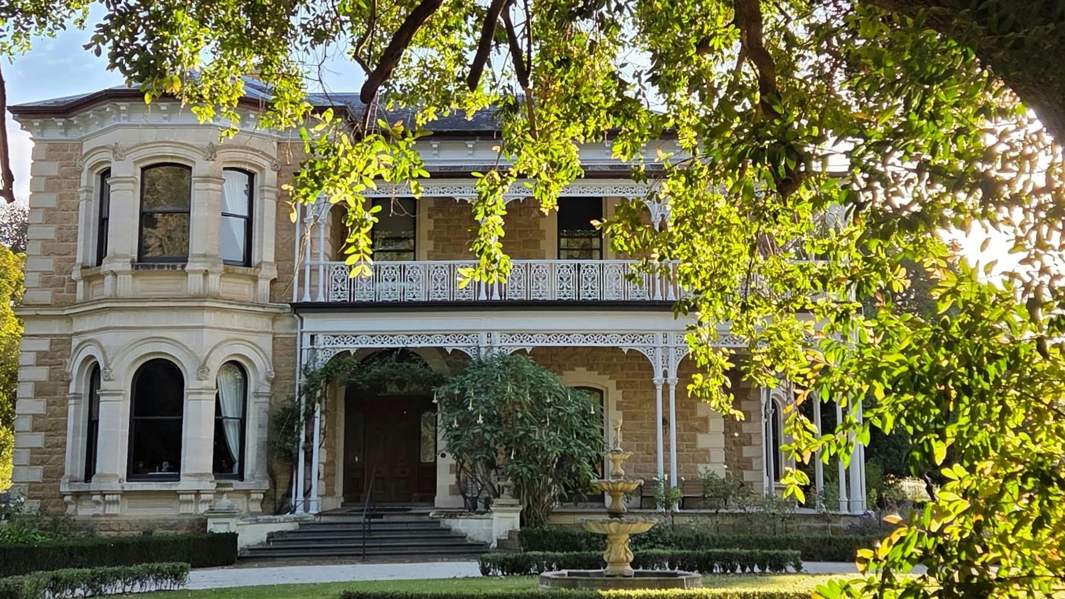 Yallum Park's Victorian mansion facade framed by tree branches, with iron lace verandahs and a garde