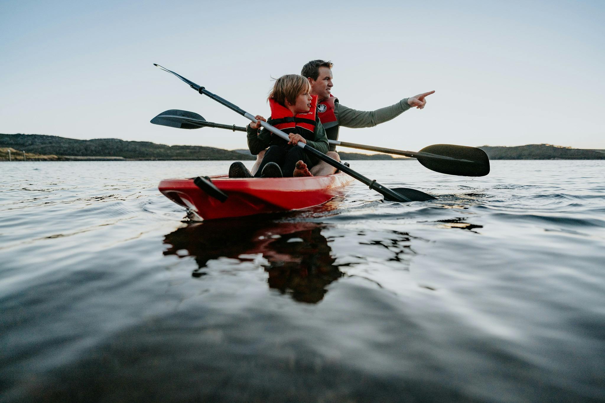A father and son sit in a a kayak together at sunrise on Rocky Valley Lake pointing at the shores
