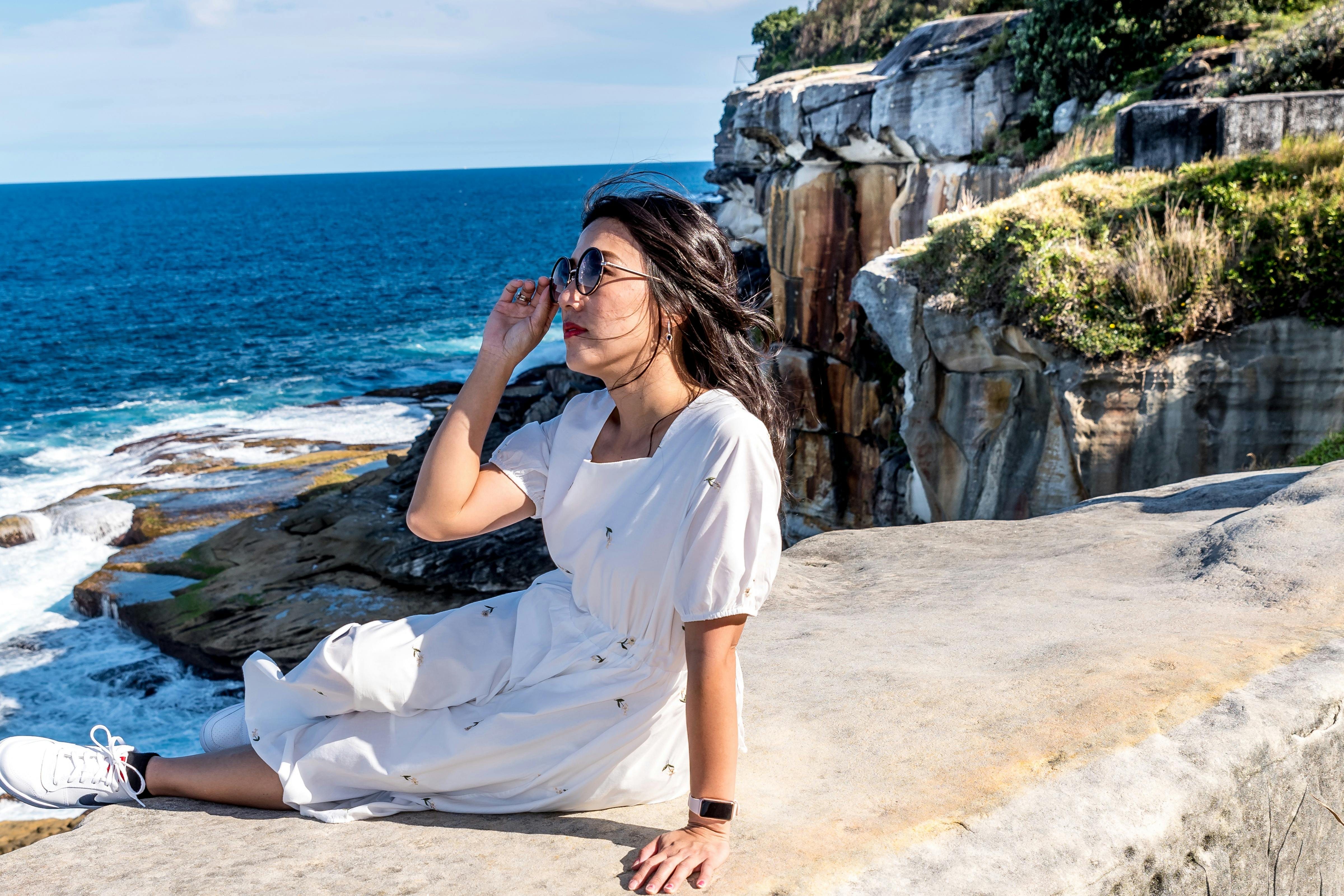 若い女性は海のそばの岩の上に座っています