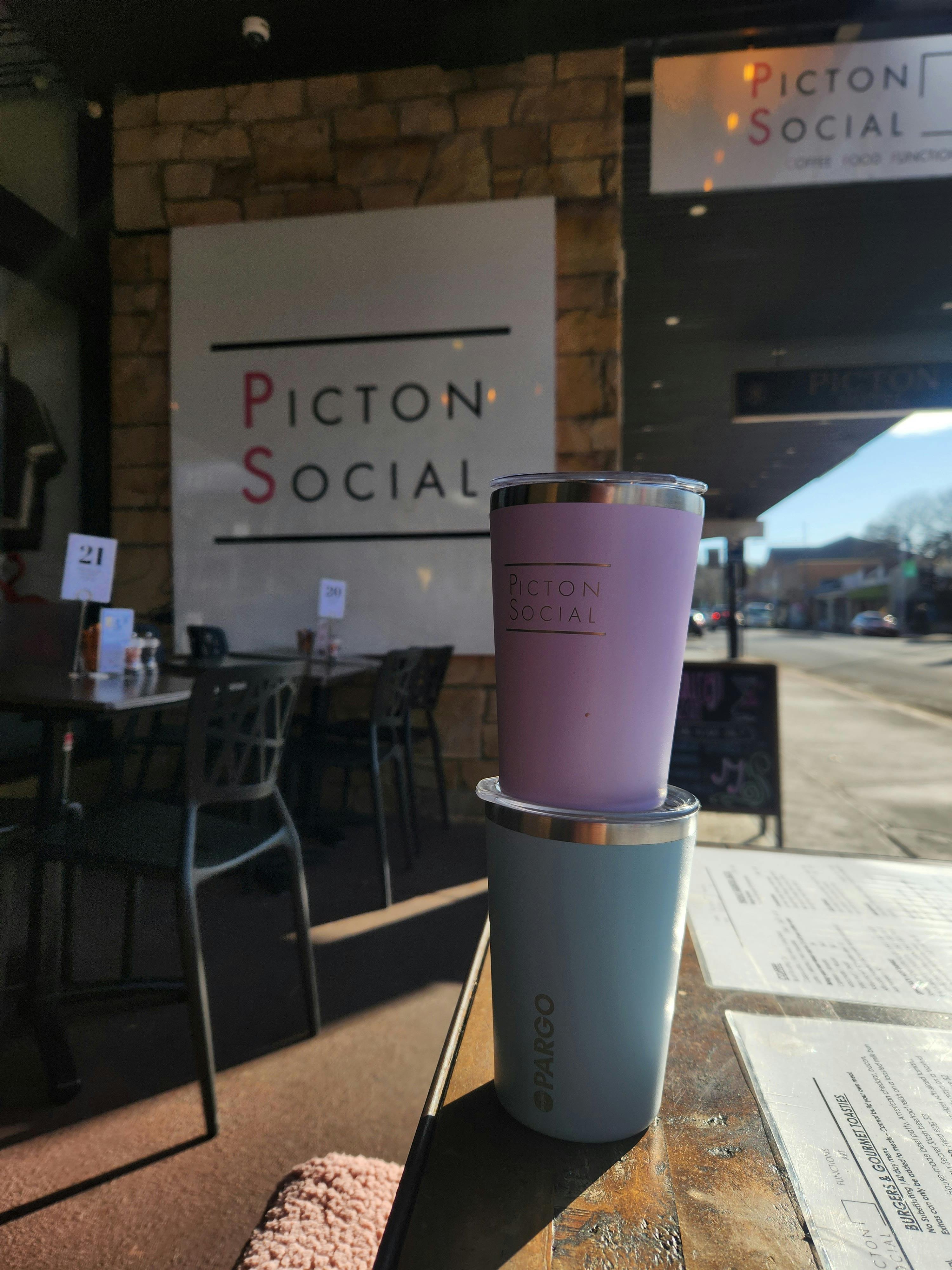 A photo of 2 Picton social x project pargo sustainable coffee cups out the front of the cafe