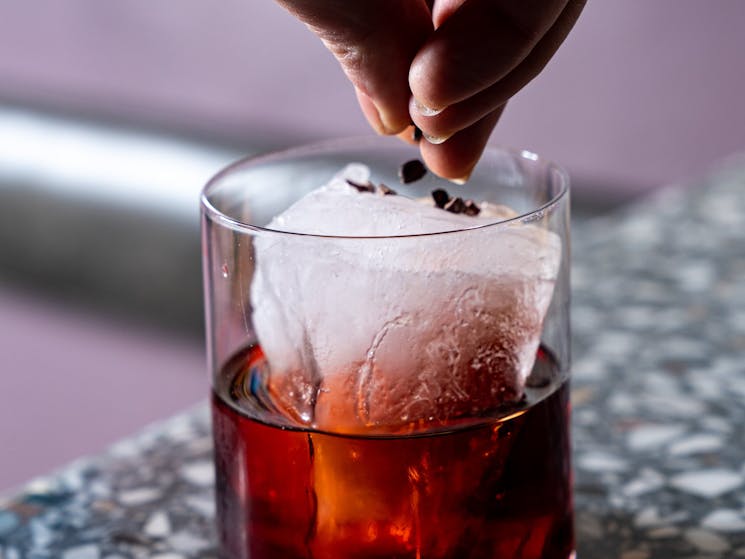 A amns hand placing a garnish on ice in a Negroni cocktail