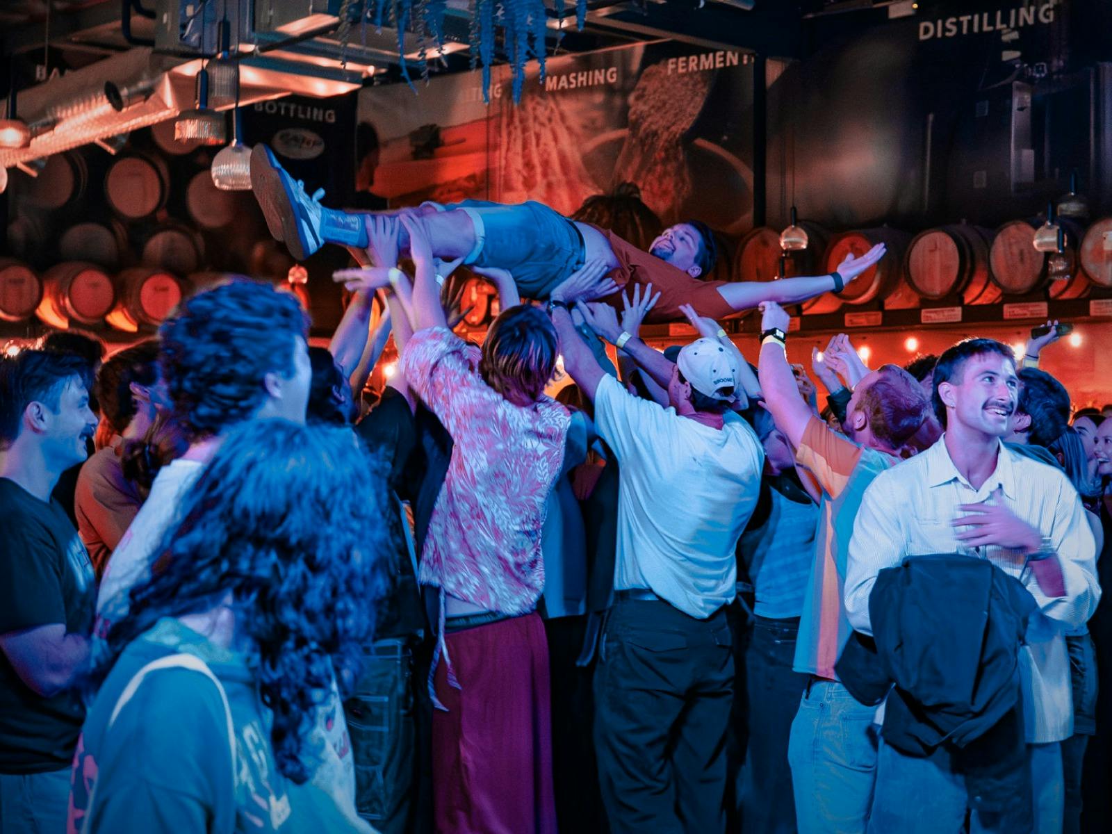 A lively group of concert goers lift an audience member above the crowd indoors at Earp Distillery