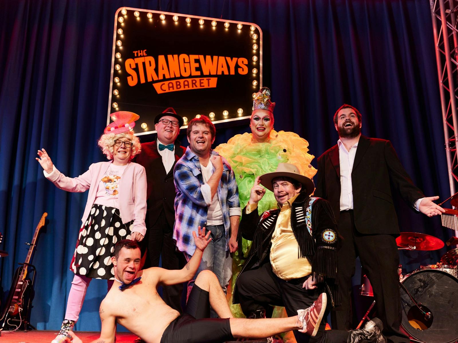 A group of people dressed in eccentric clothing standing in front of a neon sign