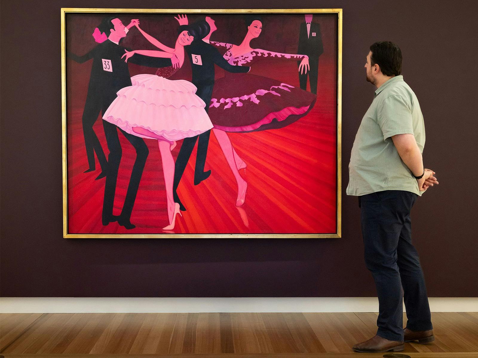 A person views a large painted portrait depicting people dancing, hanging on a gallery wall