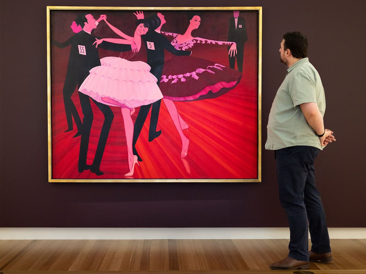 A person views a large painted portrait depicting people dancing, hanging on a gallery wall
