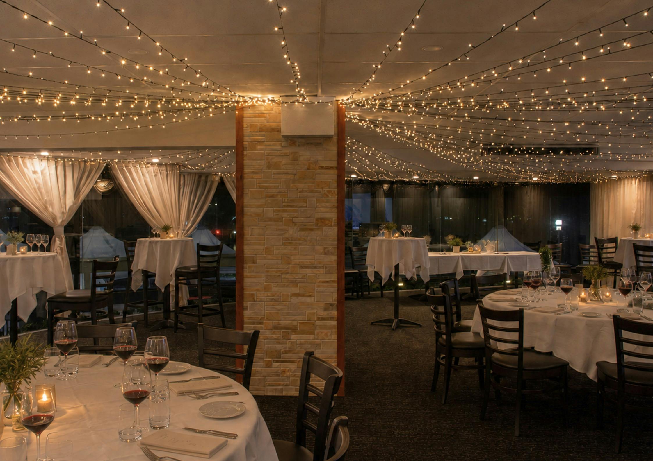 A room with fairy lights and round tables set for a dinner