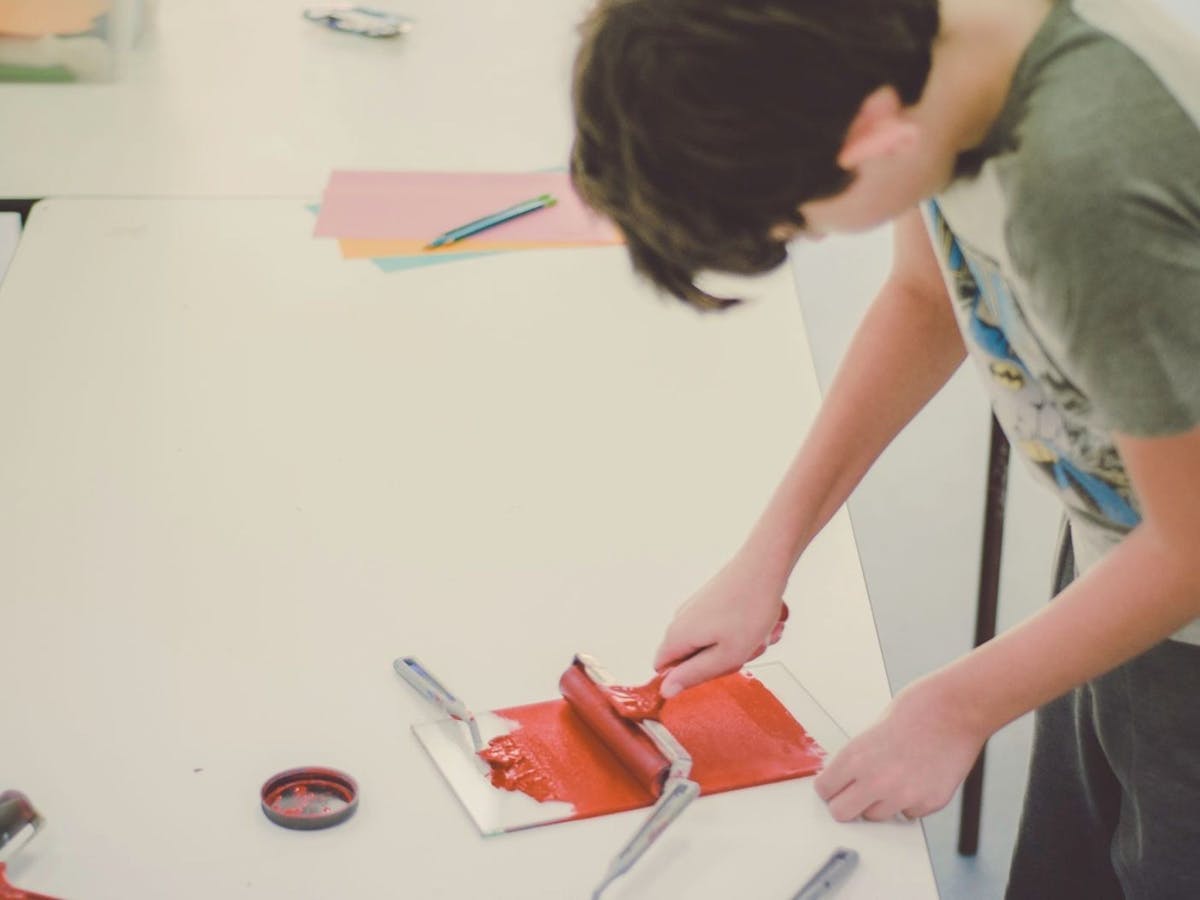 A teenage practises printmaking with a roller and red paint