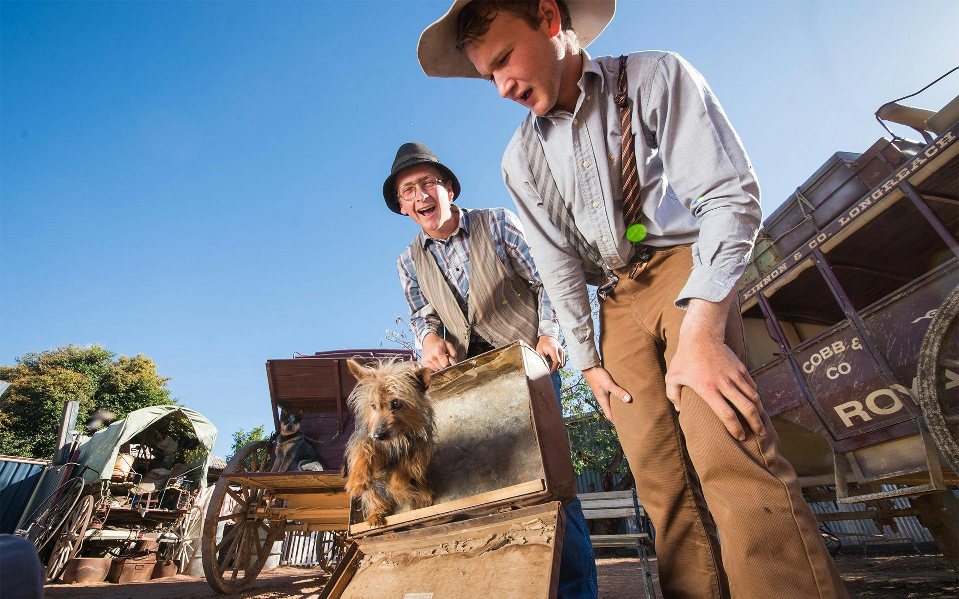 Two performers looking at a small dog standing in a briefcase