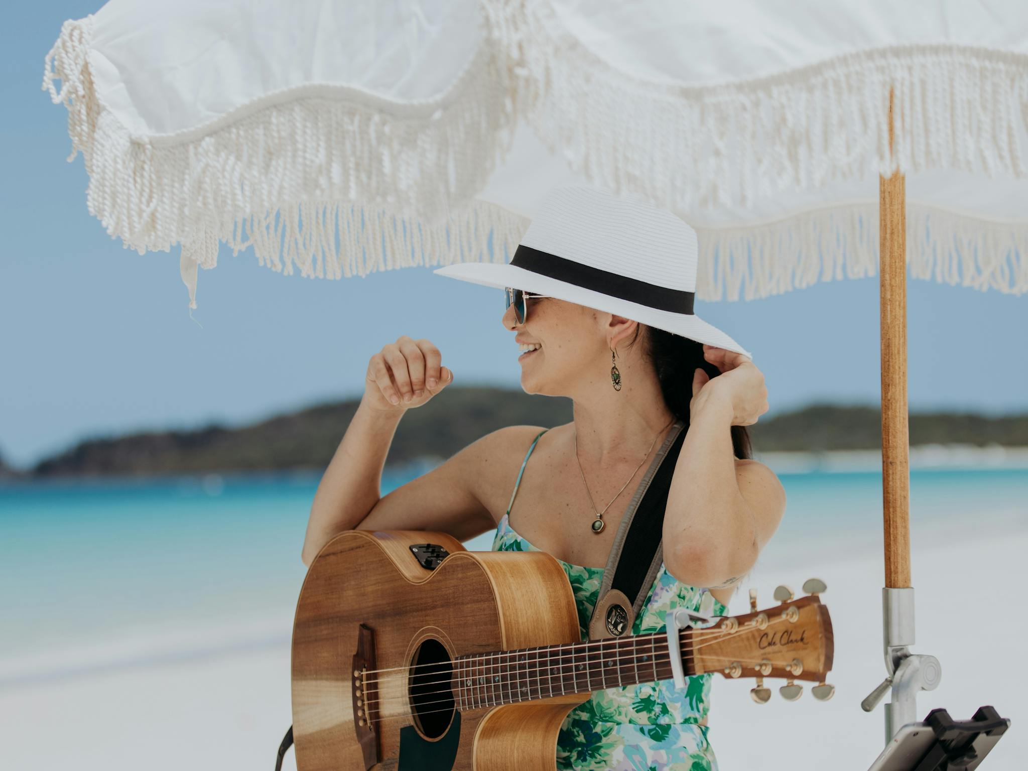 A female musician holding a guitar sitting on a stool on Whitehaven Beach underneath an umbrella A female musician holding a guitar sitting on a stool on Whitehaven Beach underneath an umbrella