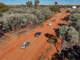 aerial shot of cars travelling in a convoy on a dirt road surrounded by Mulga trees
