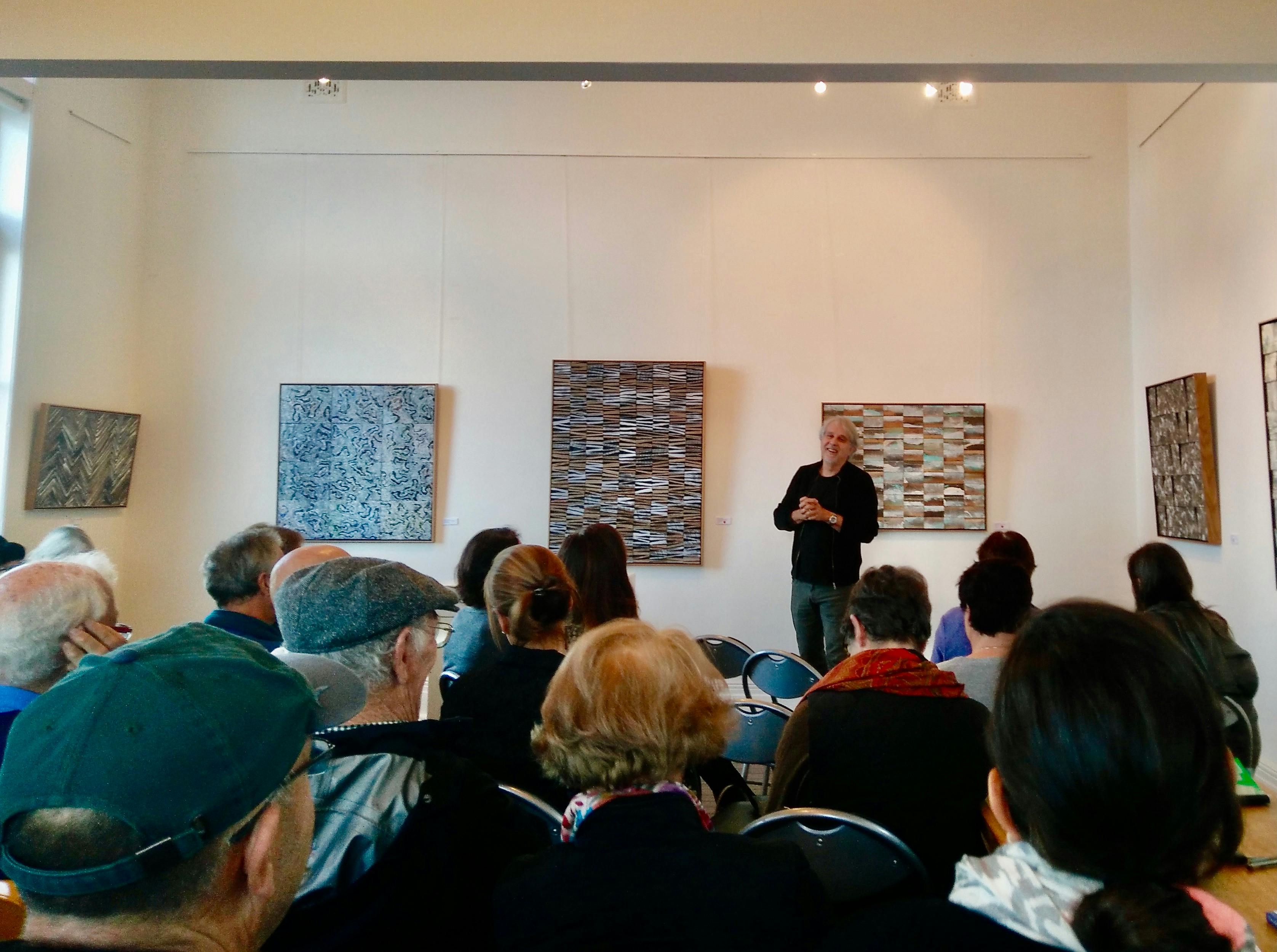 アーティストは、彼の後ろの壁に彼のアートワークを置いて、着席している聴衆に話しかけます。