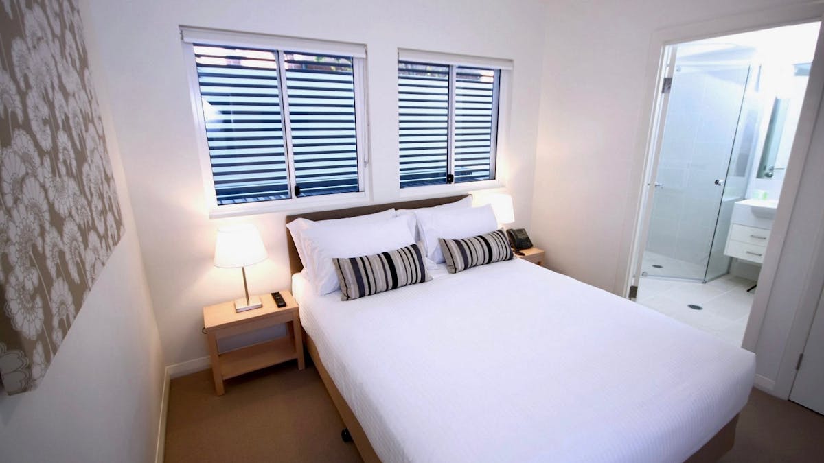 Master bedroom with queen bed, bedside lamps and ensuite shower visible through open doorway at Doma