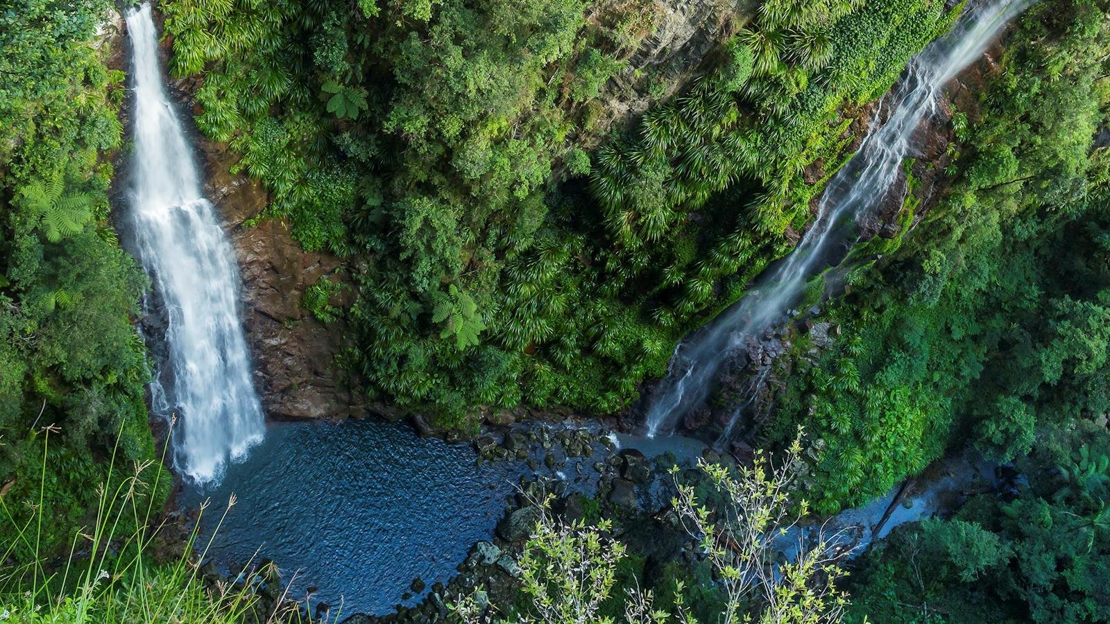 Two waterfalls tumbling down sheer rock face into gorge below. View from above.