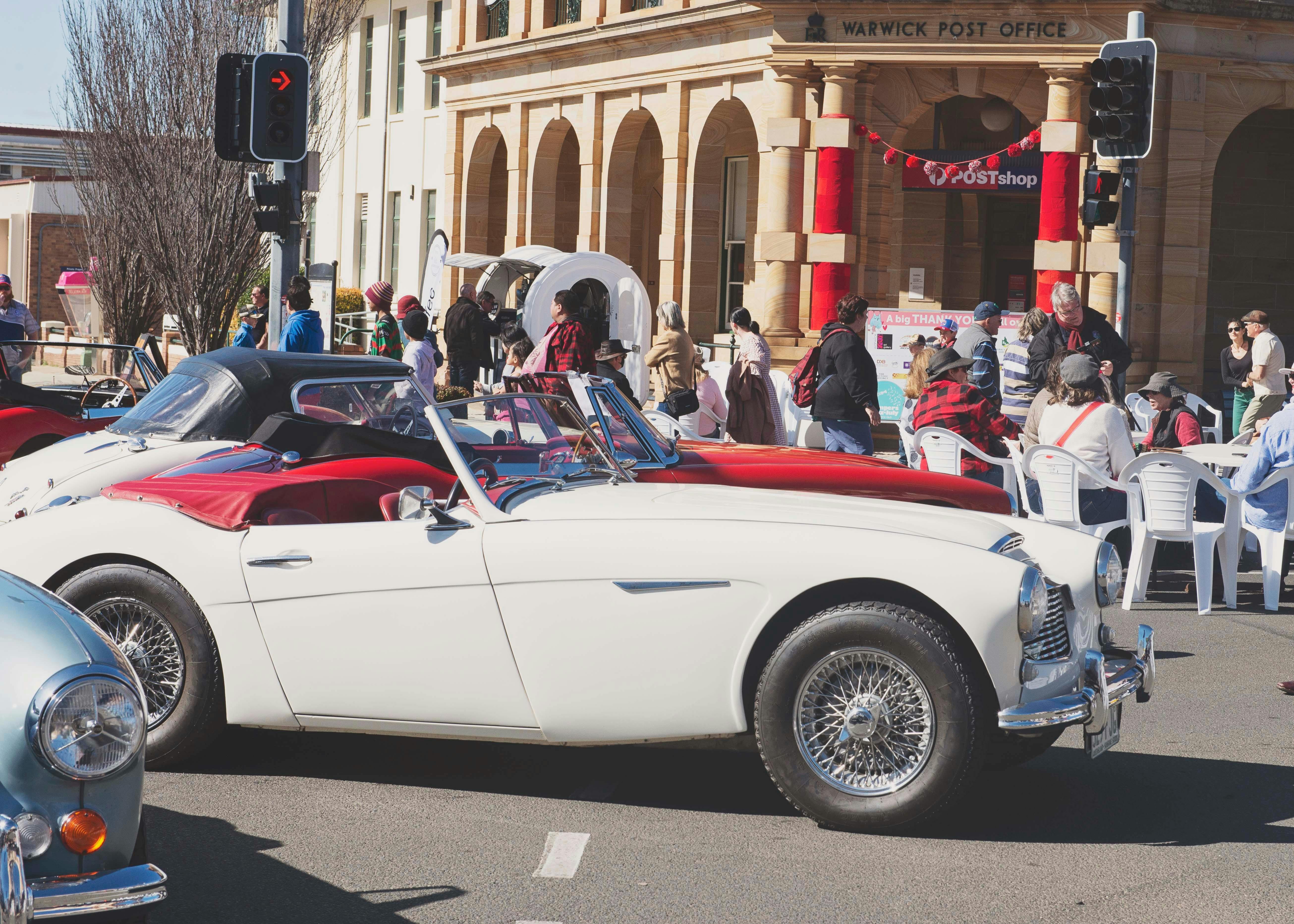 Red and White vintage cars in front of historic Post office in Warwick
