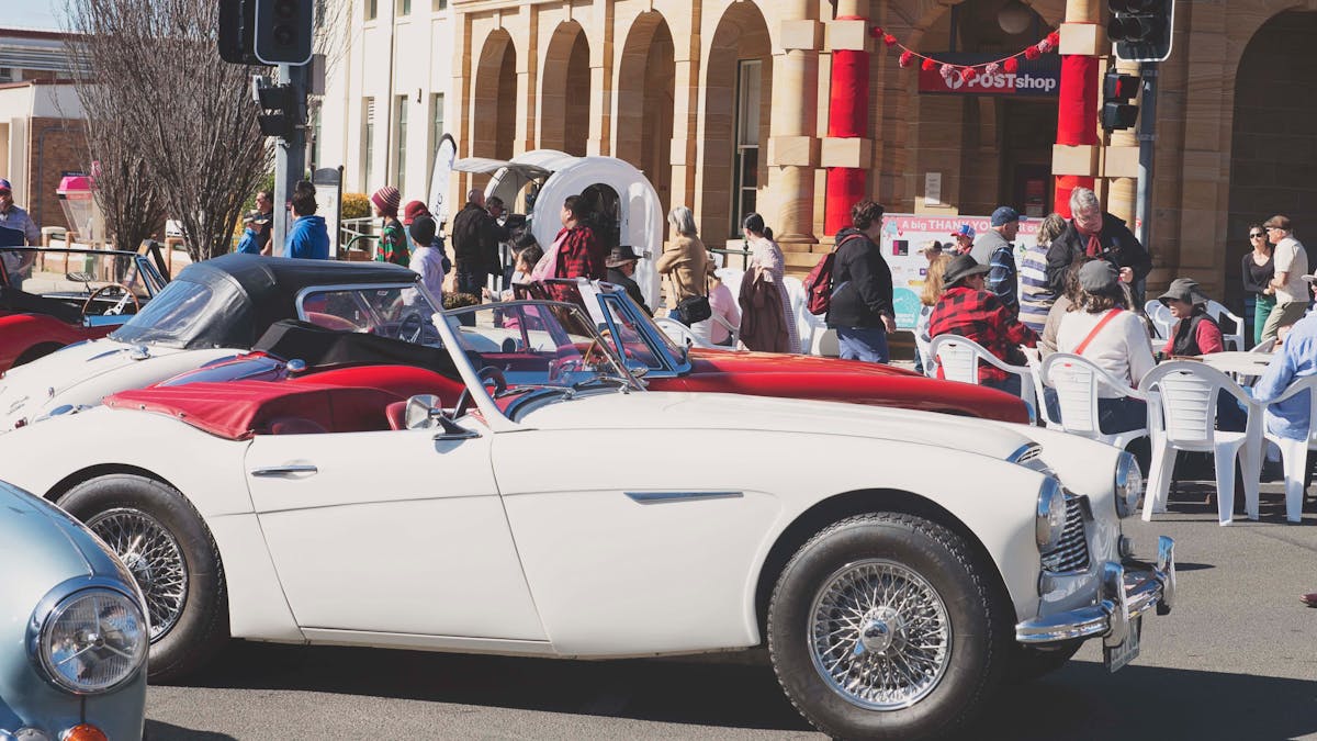 Red and White vintage cars in front of historic Post office in Warwick