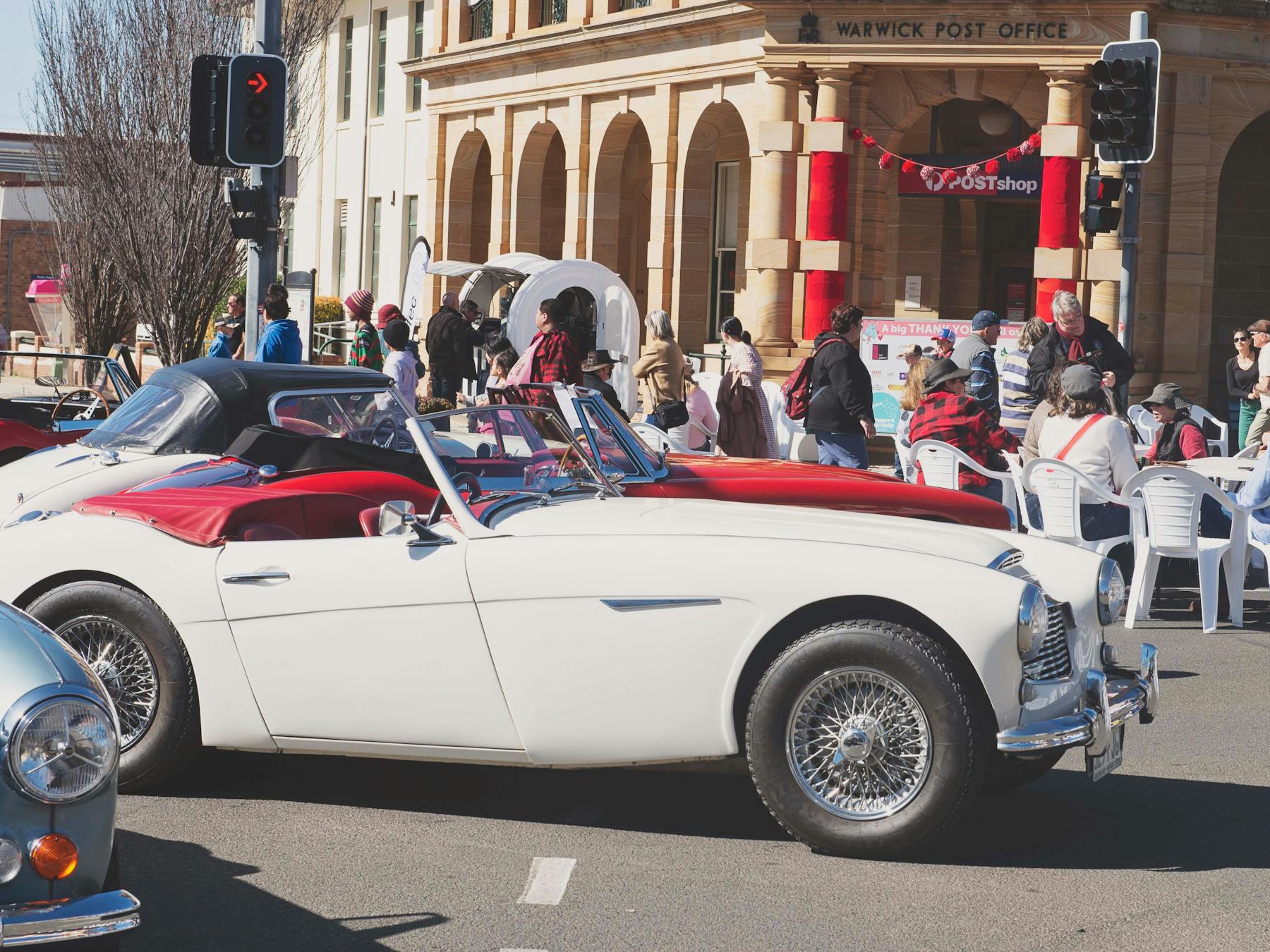 Red and White vintage cars in front of historic Post office in Warwick