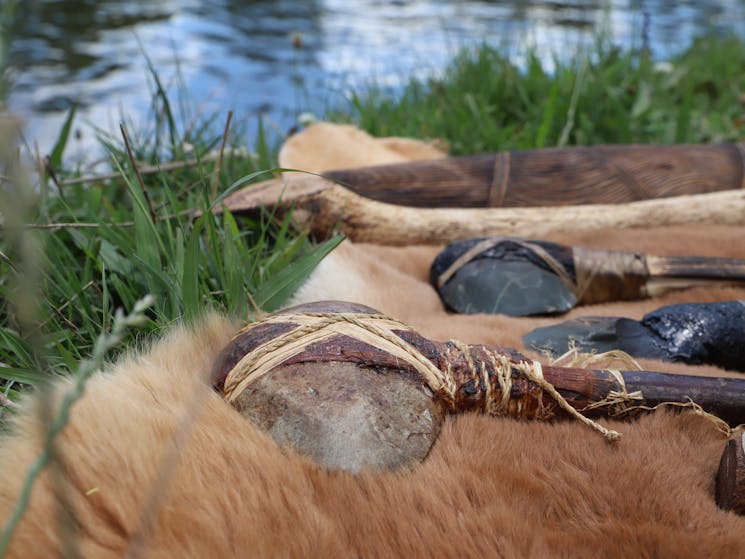 Traditional Aboriginal tools laid out on a kangaroo skin by a river.